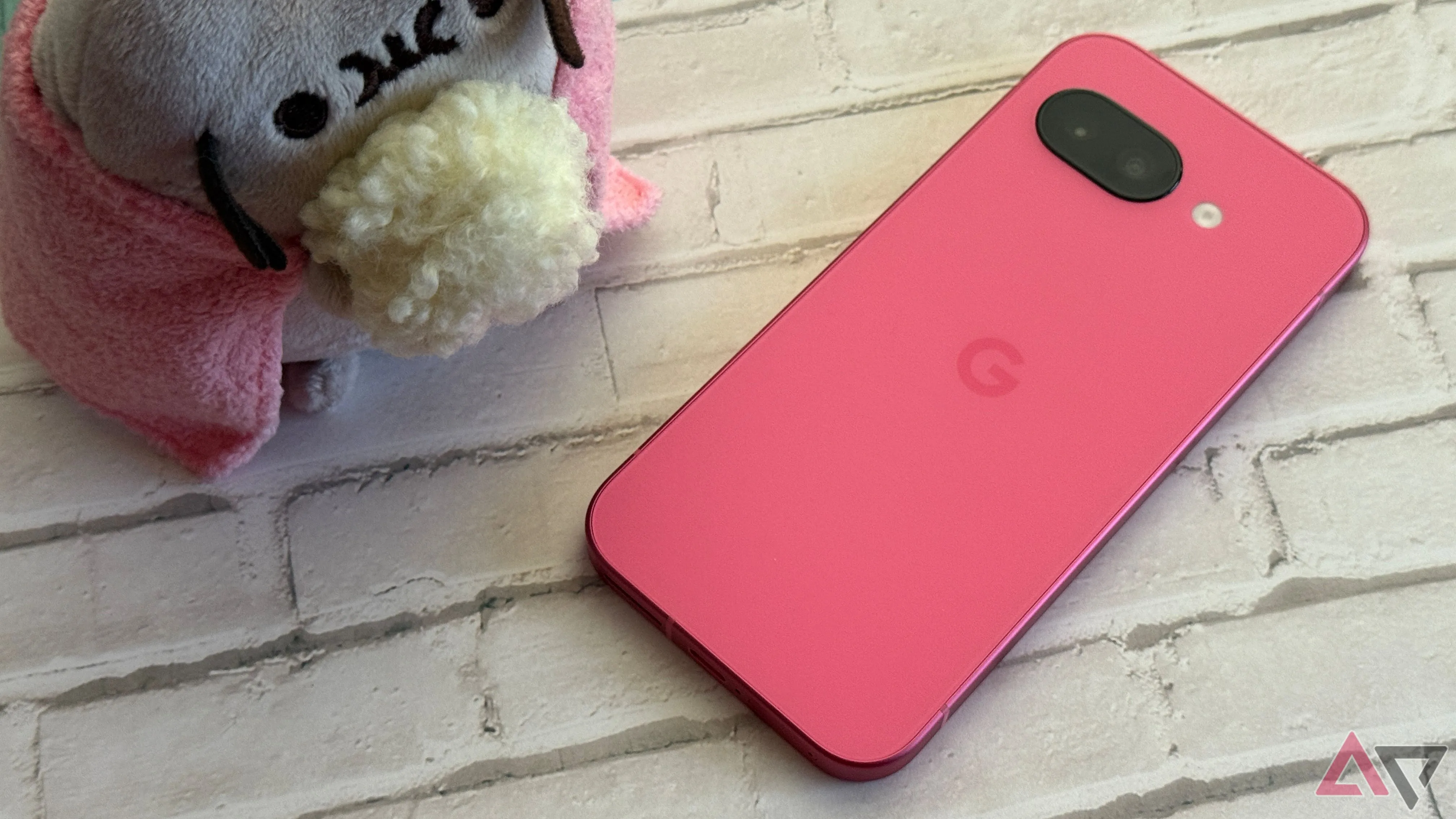 Điện thoại Google Pixel 9a màu Peony đặt cạnh đồ vật trang trí.