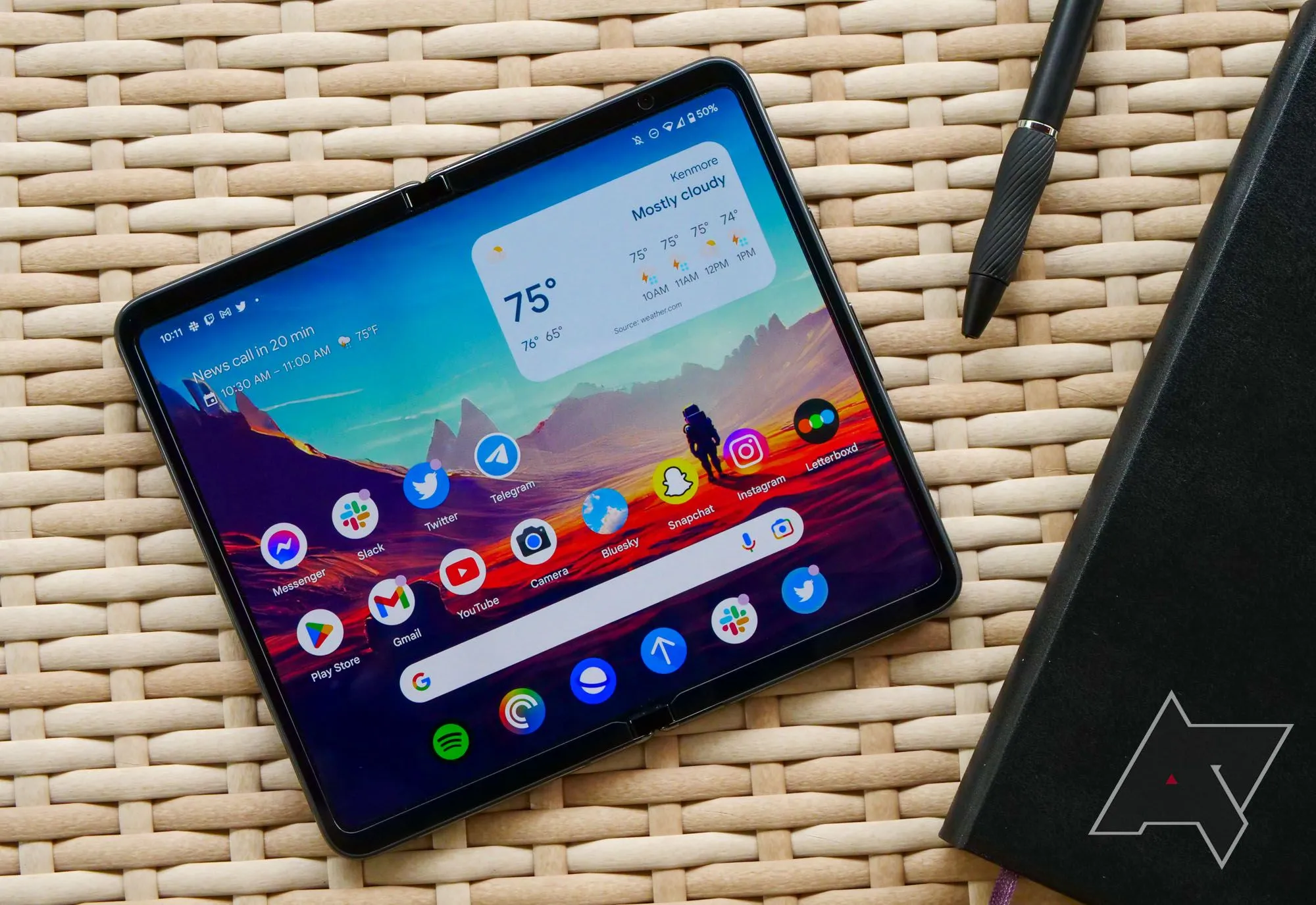 Google Pixel Fold đặt trên bàn mây cùng sổ tay và bút