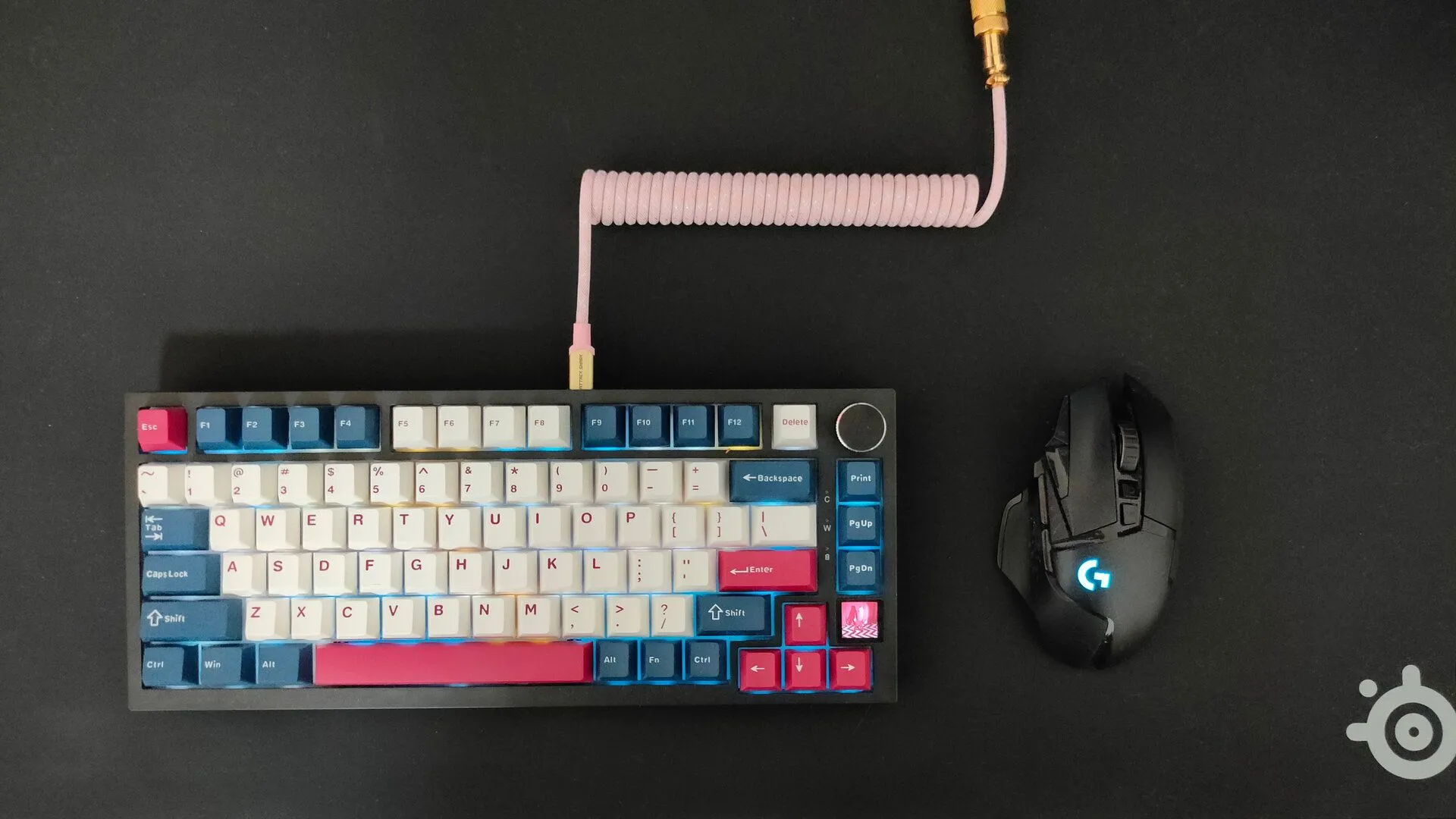Một chiếc bàn phím cơ màu đen với cáp cuộn màu hồng và chuột không dây Logitech G502 trên miếng lót chuột SteelSeries QcK Performance màu đen.