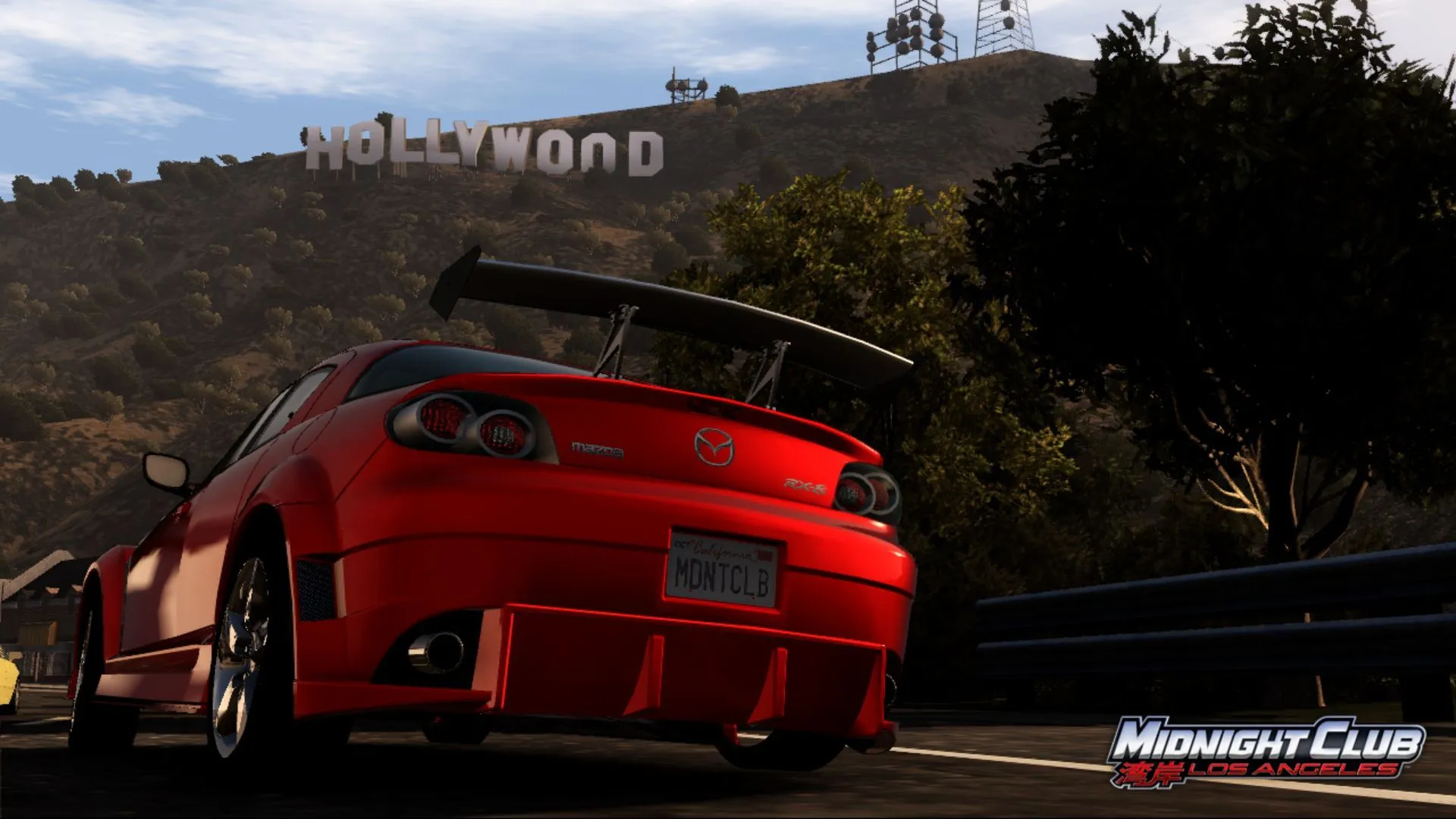 Cảnh xe Mazda màu cam đang đua trên đường phố Los Angeles trong game Midnight Club: Los Angeles, với biểu tượng Hollywood phía sau