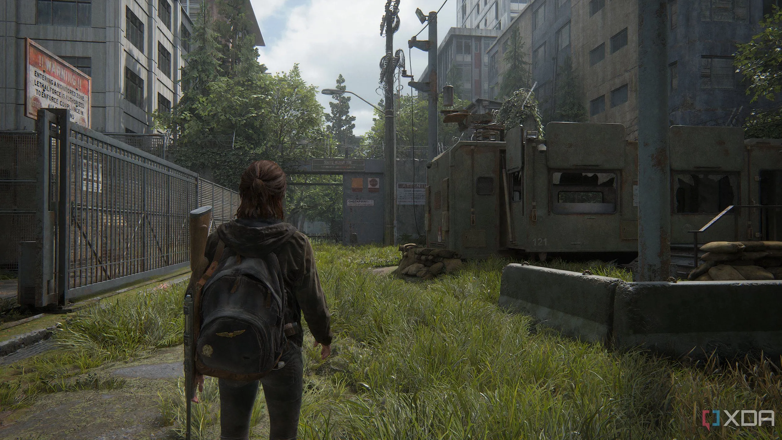 Ellie di chuyển qua một khu phức hợp quân sự đổ nát trong The Last of Us Part II Remastered trên PC, thể hiện chi tiết đồ họa môi trường ấn tượng của game.