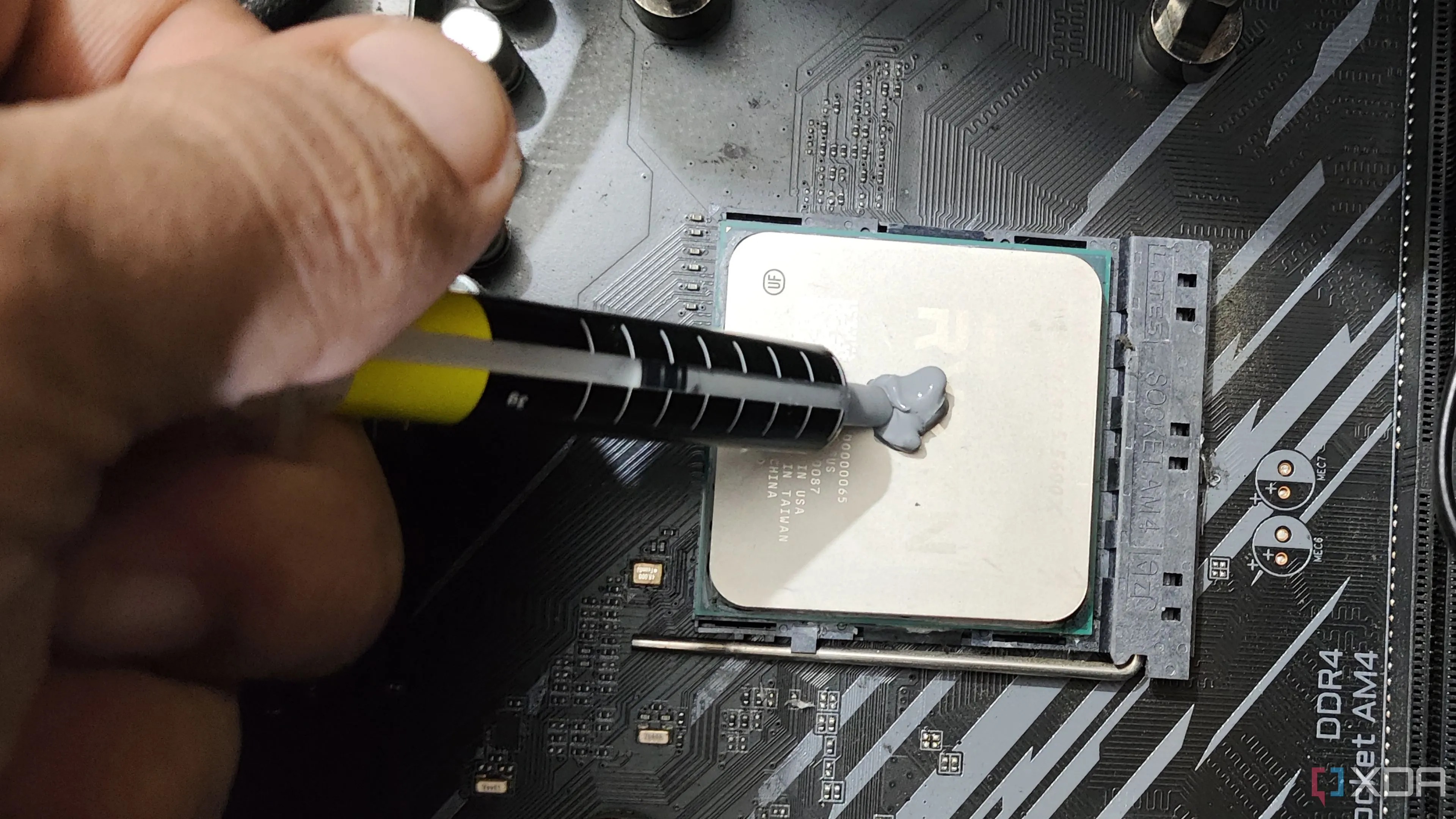 Hình ảnh một người đang bôi keo tản nhiệt mới lên CPU AMD Ryzen 5 5600X, quy trình quan trọng giúp giảm nhiệt độ và tăng hiệu năng PC gaming.
