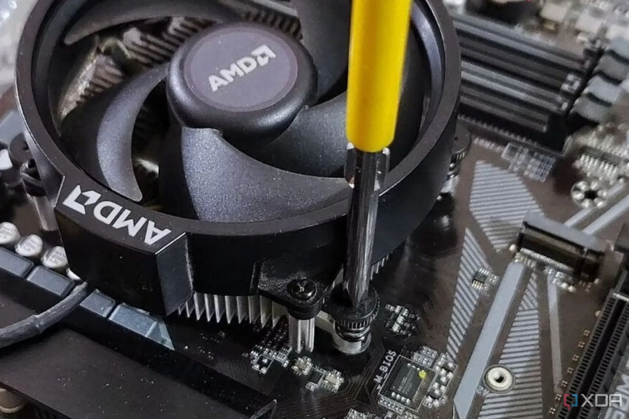 Người dùng đang vặn ốc cố định tản nhiệt stock của AMD vào bo mạch chủ bằng tuốc nơ vít, minh họa cho nhu cầu về các dụng cụ lắp ráp PC.